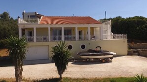 A two-story house with a balcony, a boat on a trailer, and palm trees in the foreground.