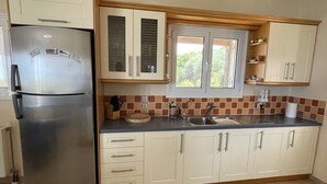 A kitchen with a stainless steel refrigerator, a window with blinds, a sink, and cabinets.