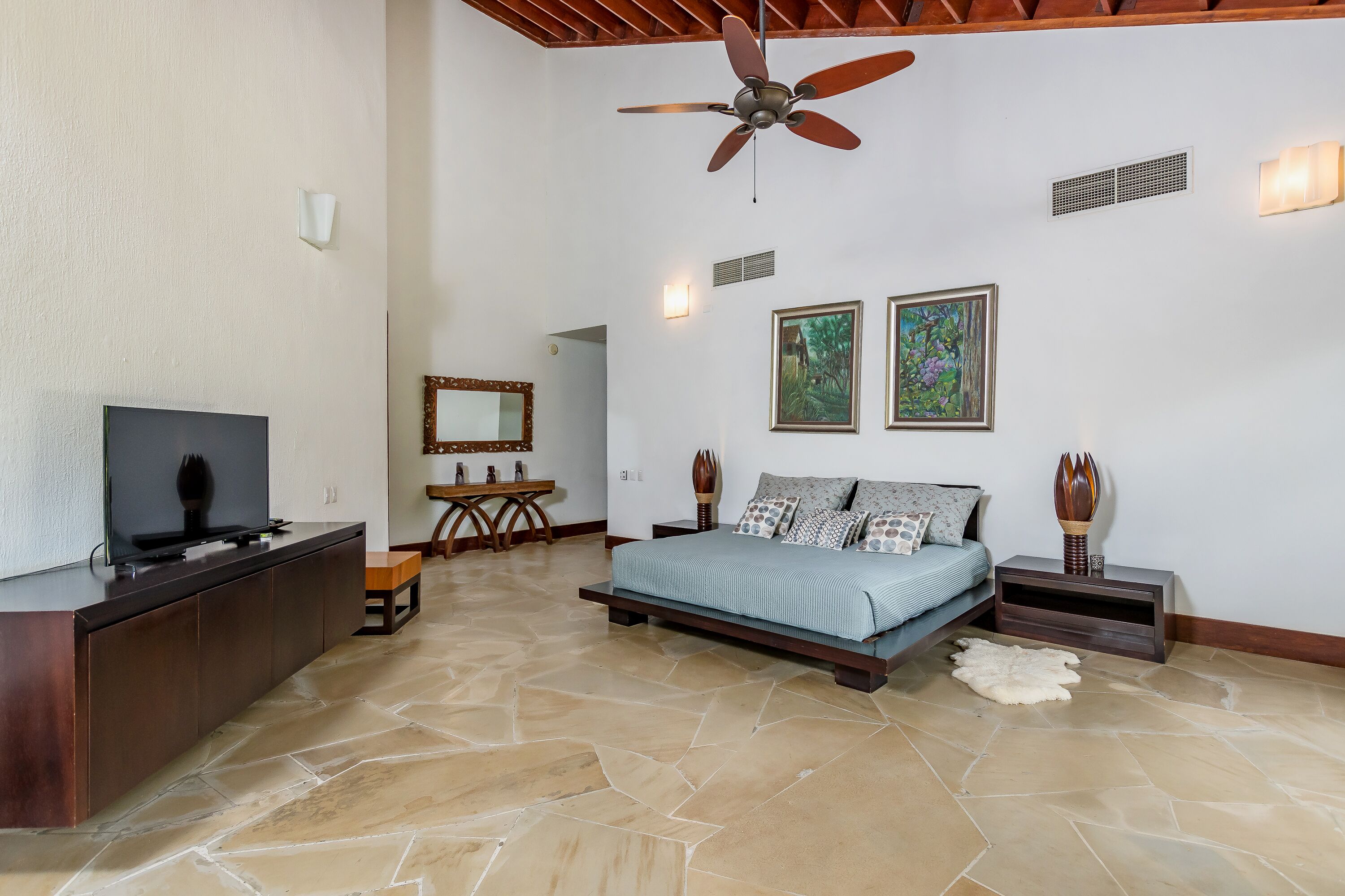 A spacious bedroom with a large bed, a TV, and a ceiling fan.
