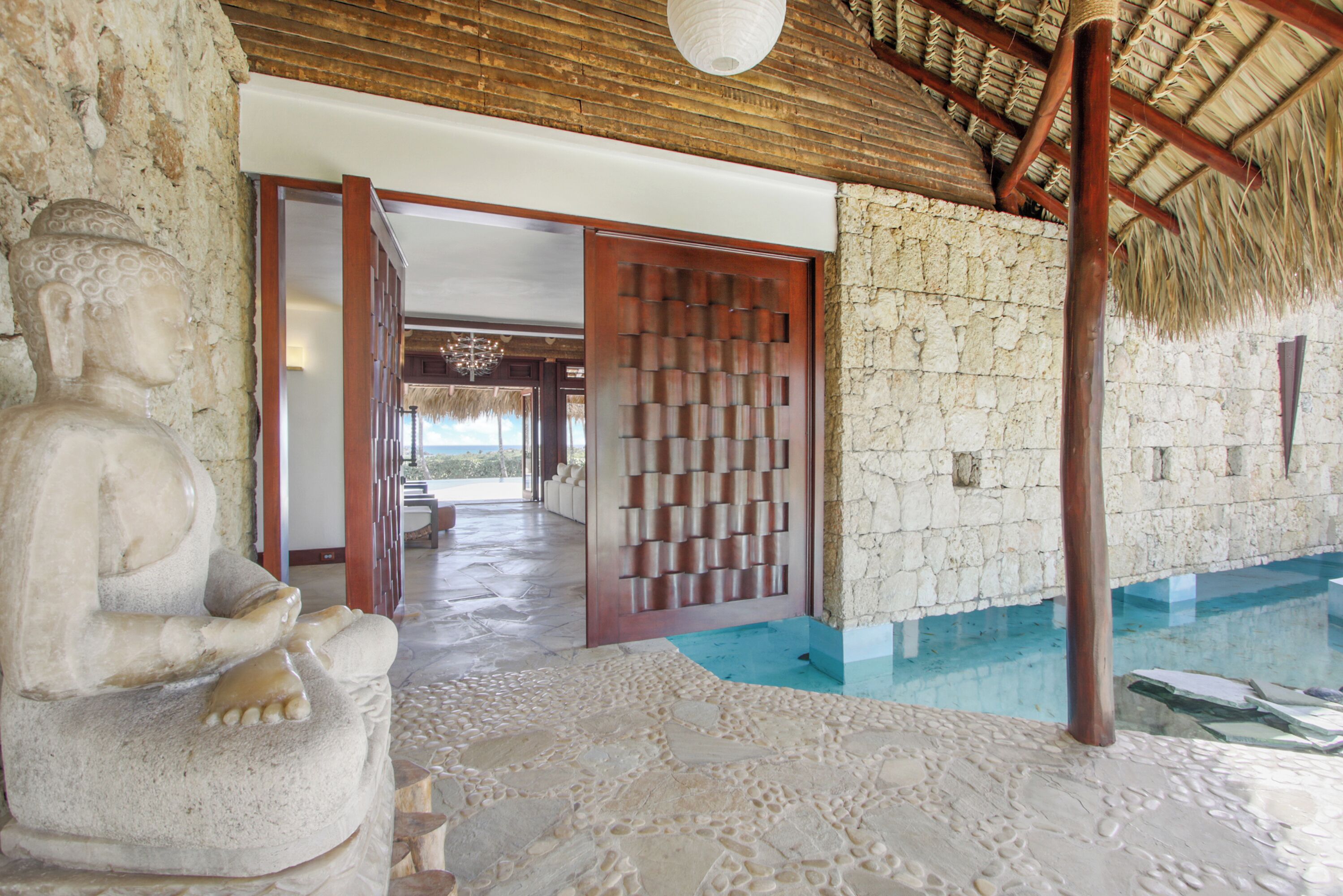 A stone Buddha statue, a wooden door, and a pool area with a thatched roof.