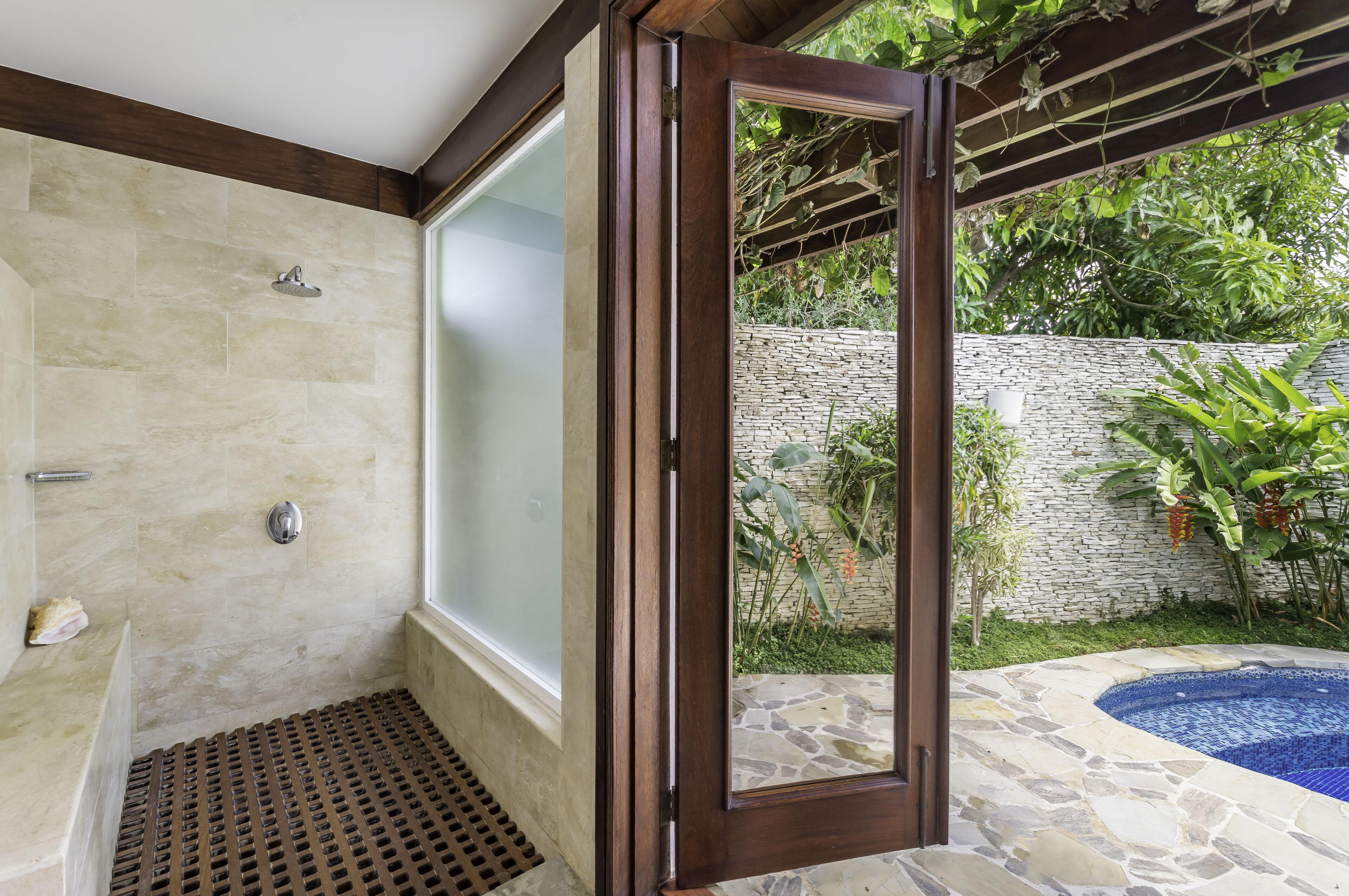 Une salle de bain équipée d’une douche, d’une baignoire et d’une porte vitrée donnant sur un jardin avec un jacuzzi.