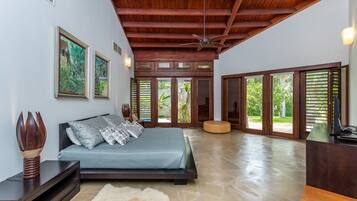 A spacious bedroom with a large bed, wooden ceiling beams, and a view to the outside.