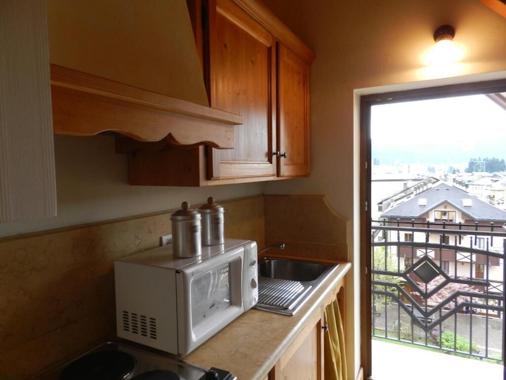 Een kleine keuken met houten kastjes, een magnetron en een spoelbak.