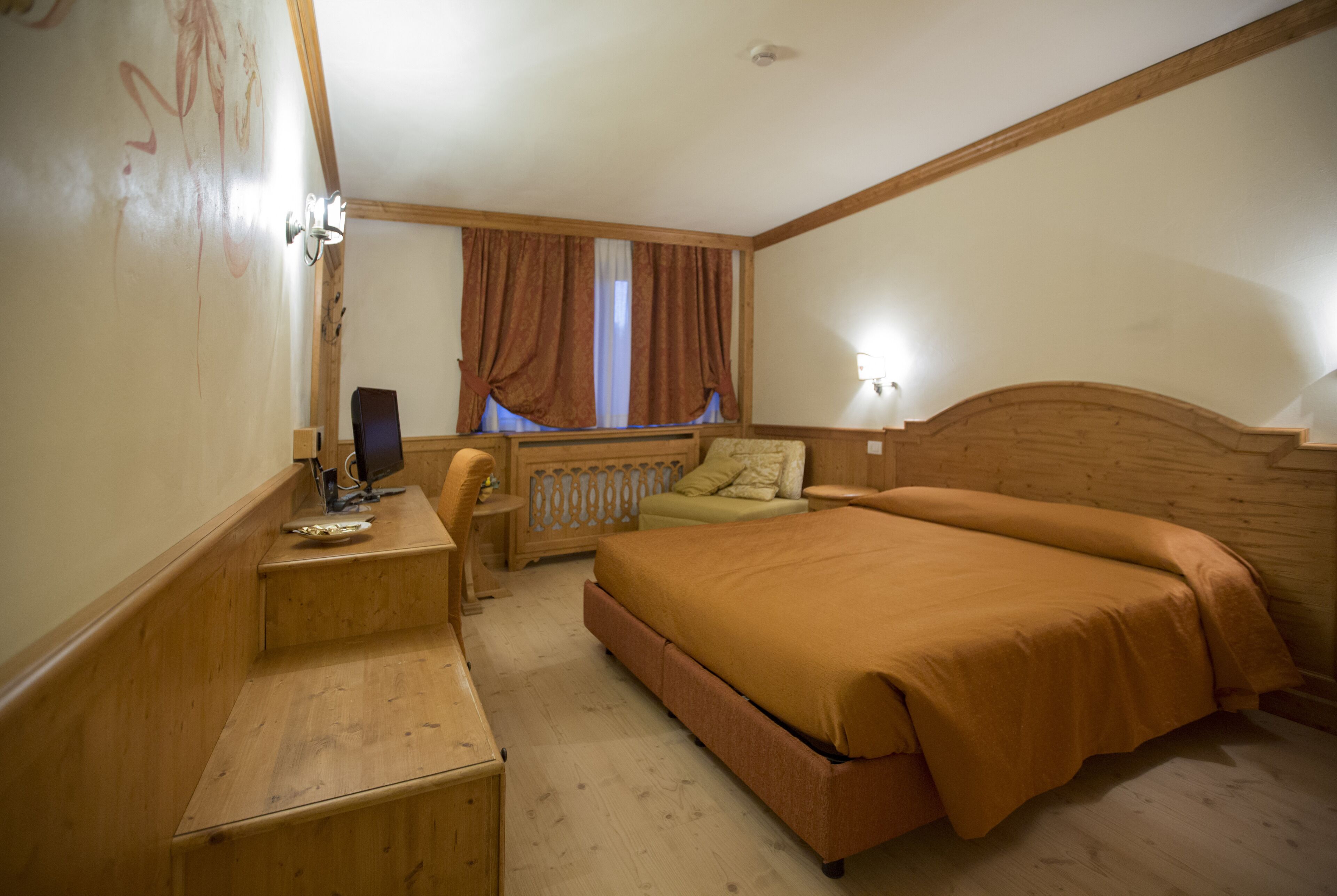 A hotel room with a wooden bed, a desk with a computer, a chair, and a window with curtains.