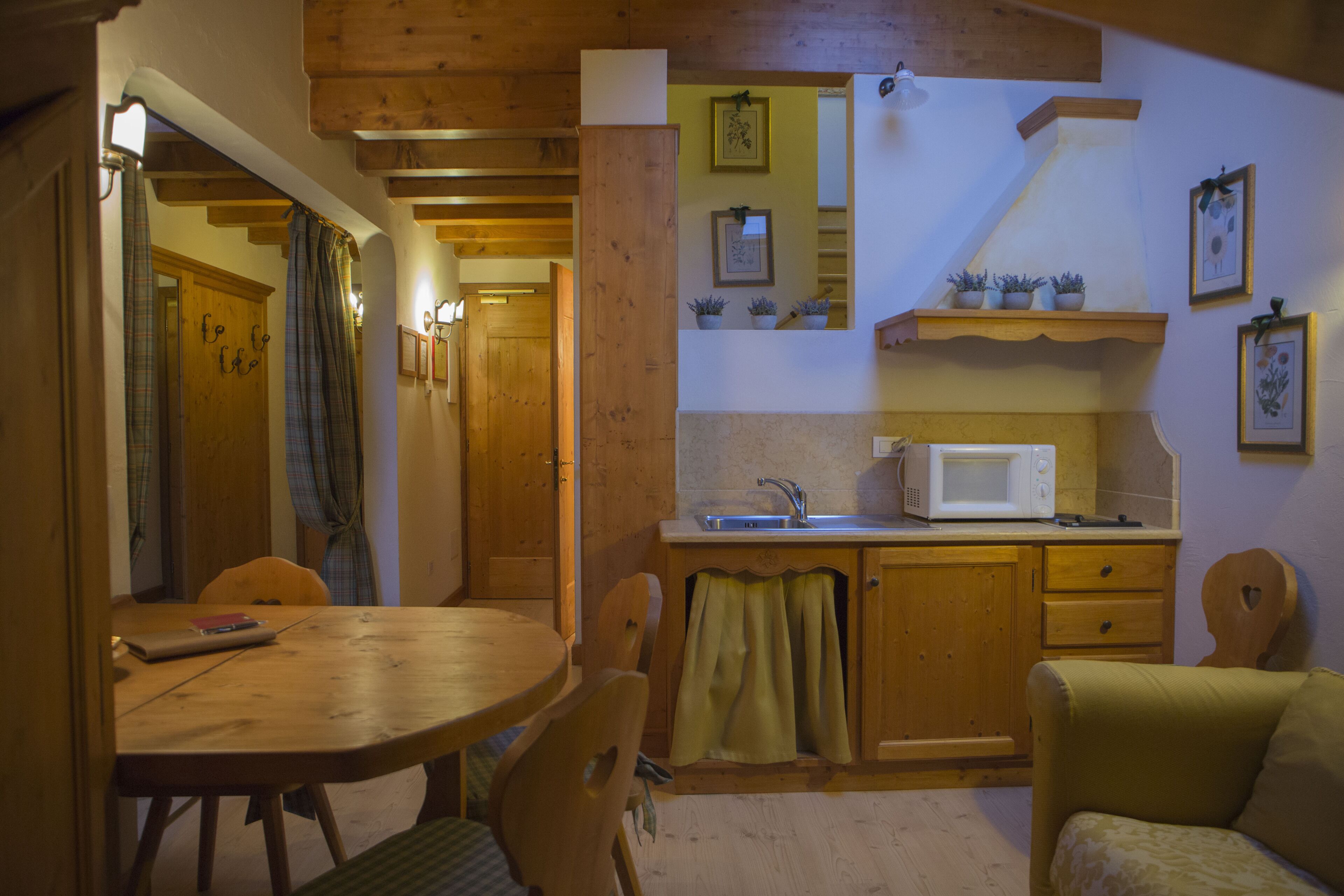 A cozy kitchen with wooden cabinets, a microwave, and a sink. There is a dining table with chairs and a small sofa.