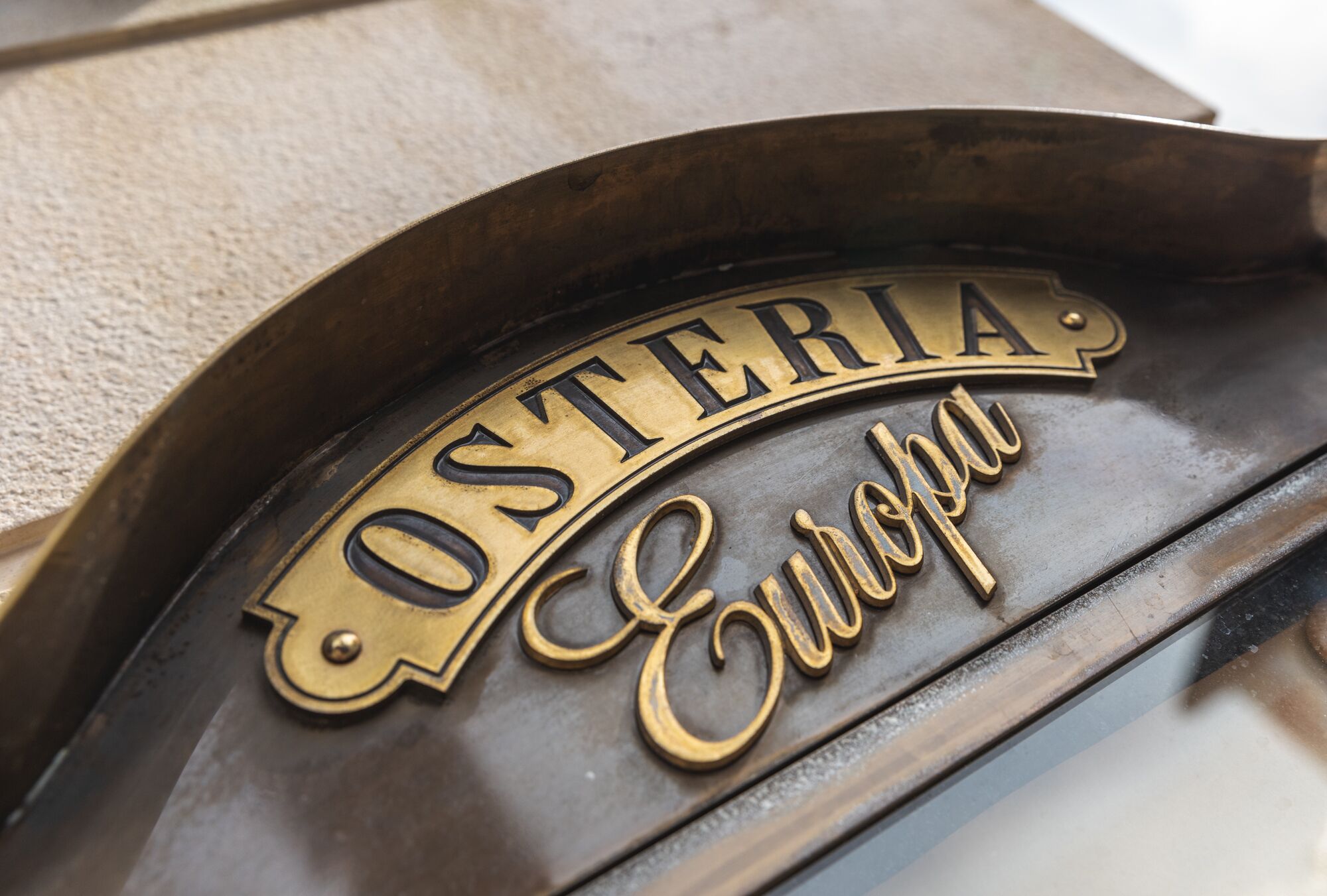 A brass plaque with the inscription "OSTERIA Europa" on a dark, curved surface.