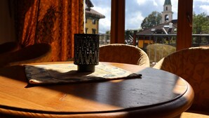 Uma mesa de madeira com um castiçal estampado e um mapa, ao lado de uma janela que oferece vista para o topo de uma igreja.