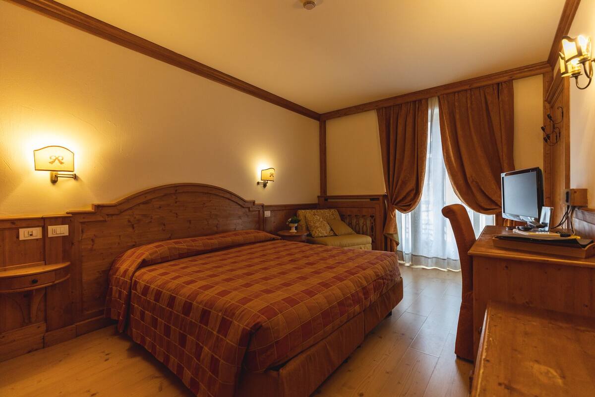 A hotel room with a wooden bed, a desk with a computer, and a window with curtains.