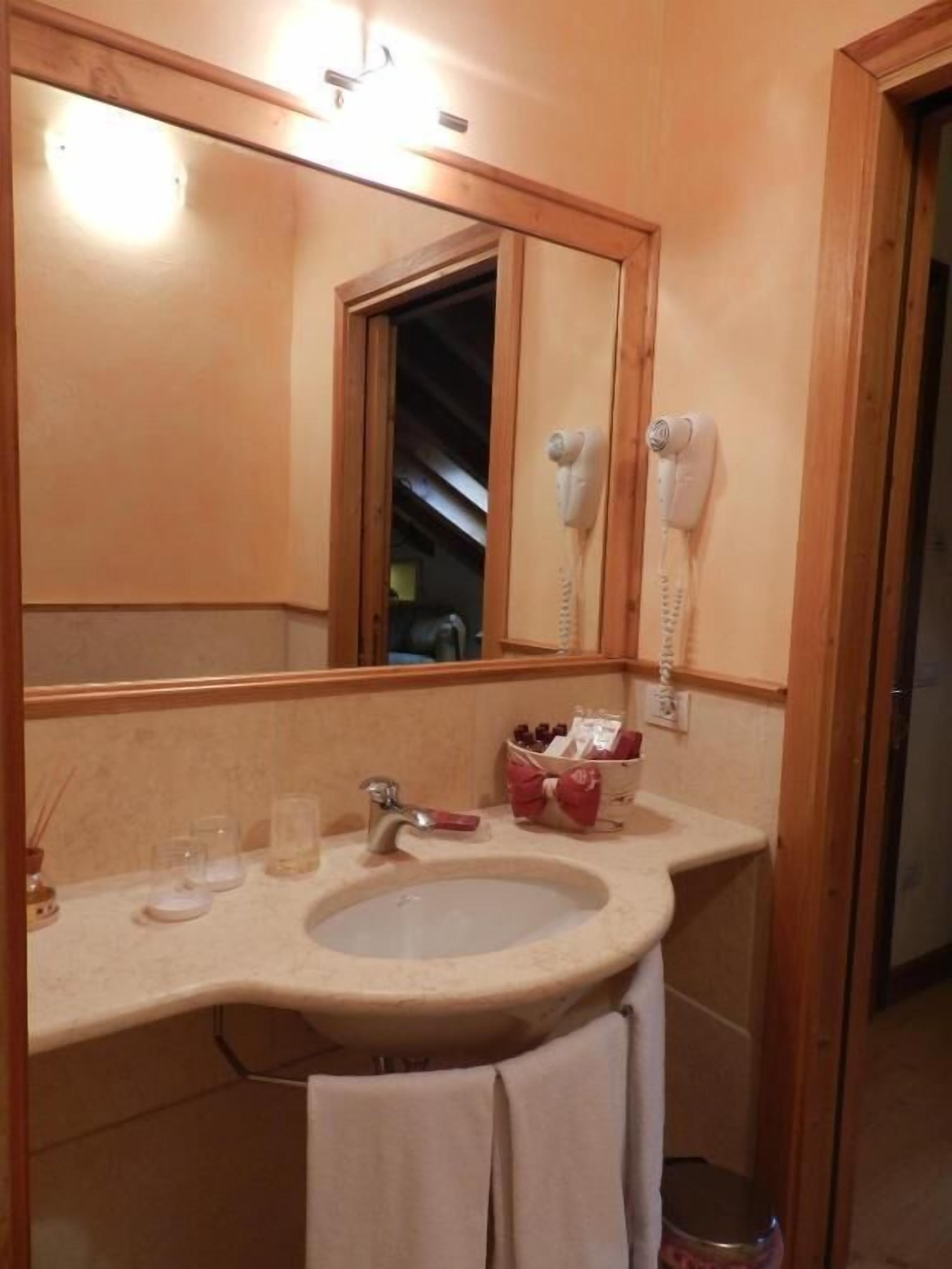 Casa de banho com lavatório, espelho e secador de cabelo fixado na parede.