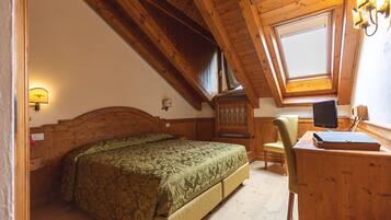 A bedroom with a wooden ceiling, a bed with a patterned bedspread, a desk with a computer, and a window with a view.
