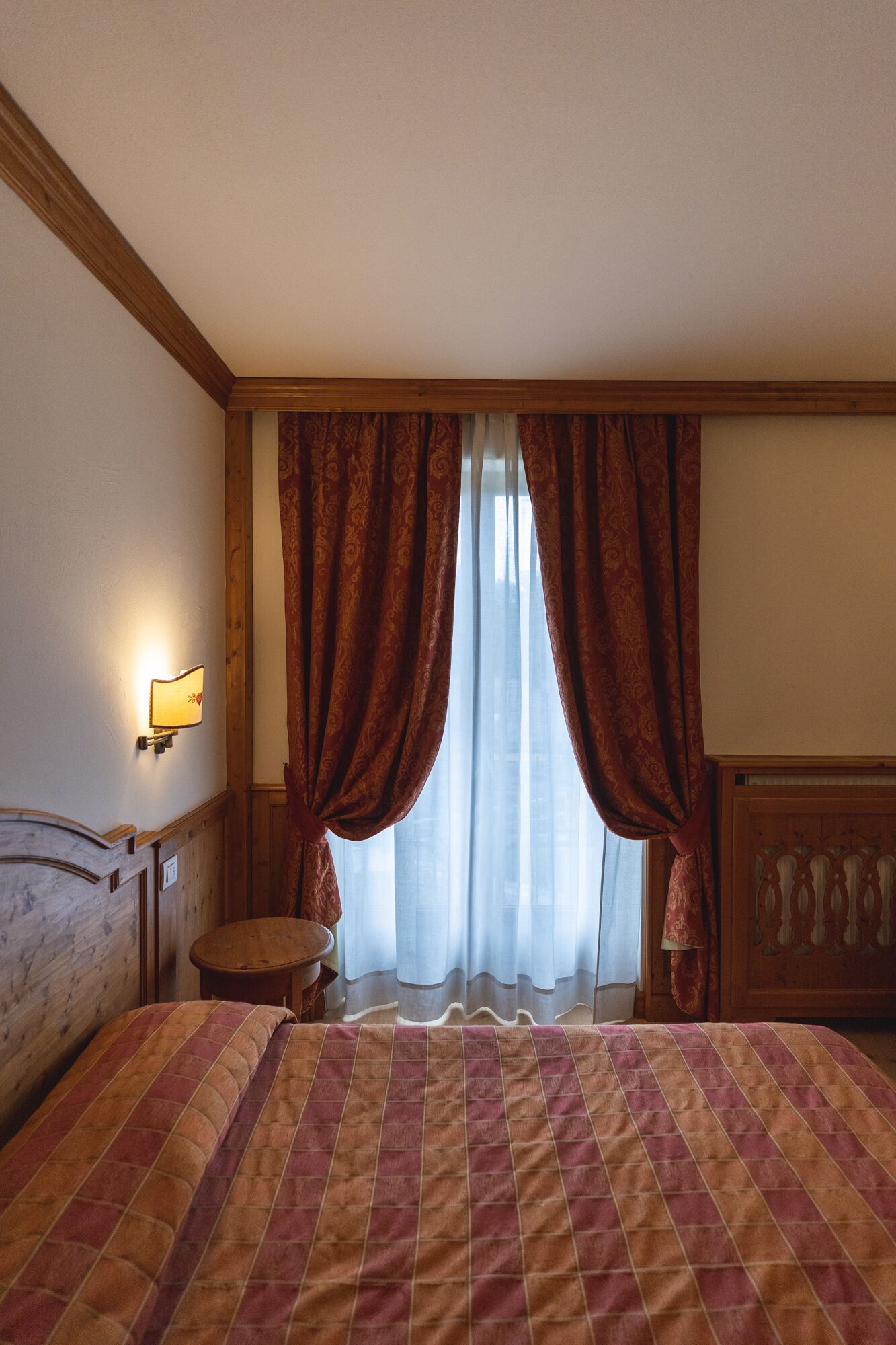 A hotel room with a bed, a nightstand, a lamp, and a window with curtains.