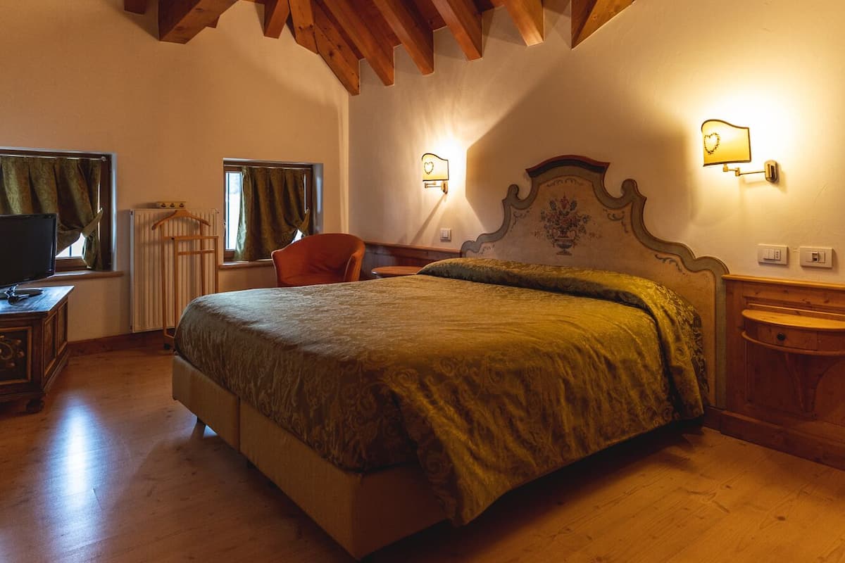 A bedroom with a wooden ceiling, a bed, a dresser, a chair, and two wall-mounted lamps.