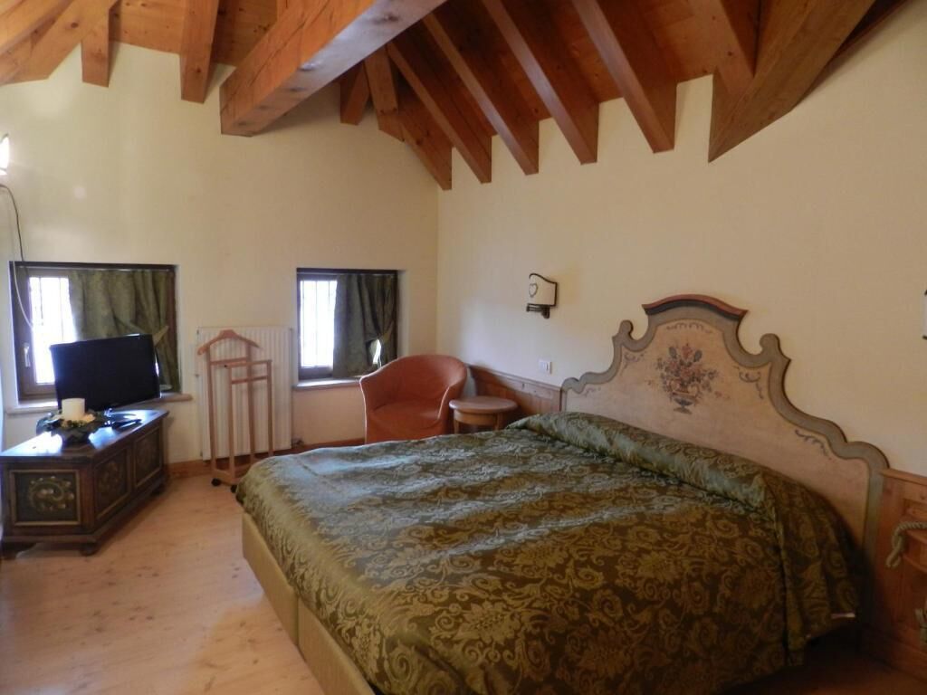 A bedroom with a wooden ceiling, a bed with a patterned bedspread, a dresser, a chair, and a television.