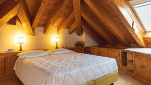 Quarto com teto de madeira, uma cama, mesas de cabeceira e uma janela.