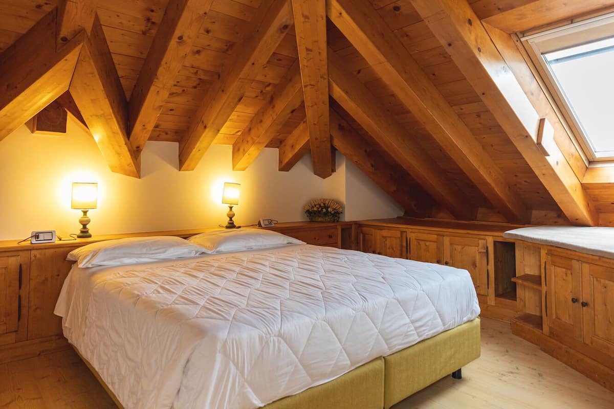 A bedroom with a wooden ceiling, a bed, bedside tables, and a window.