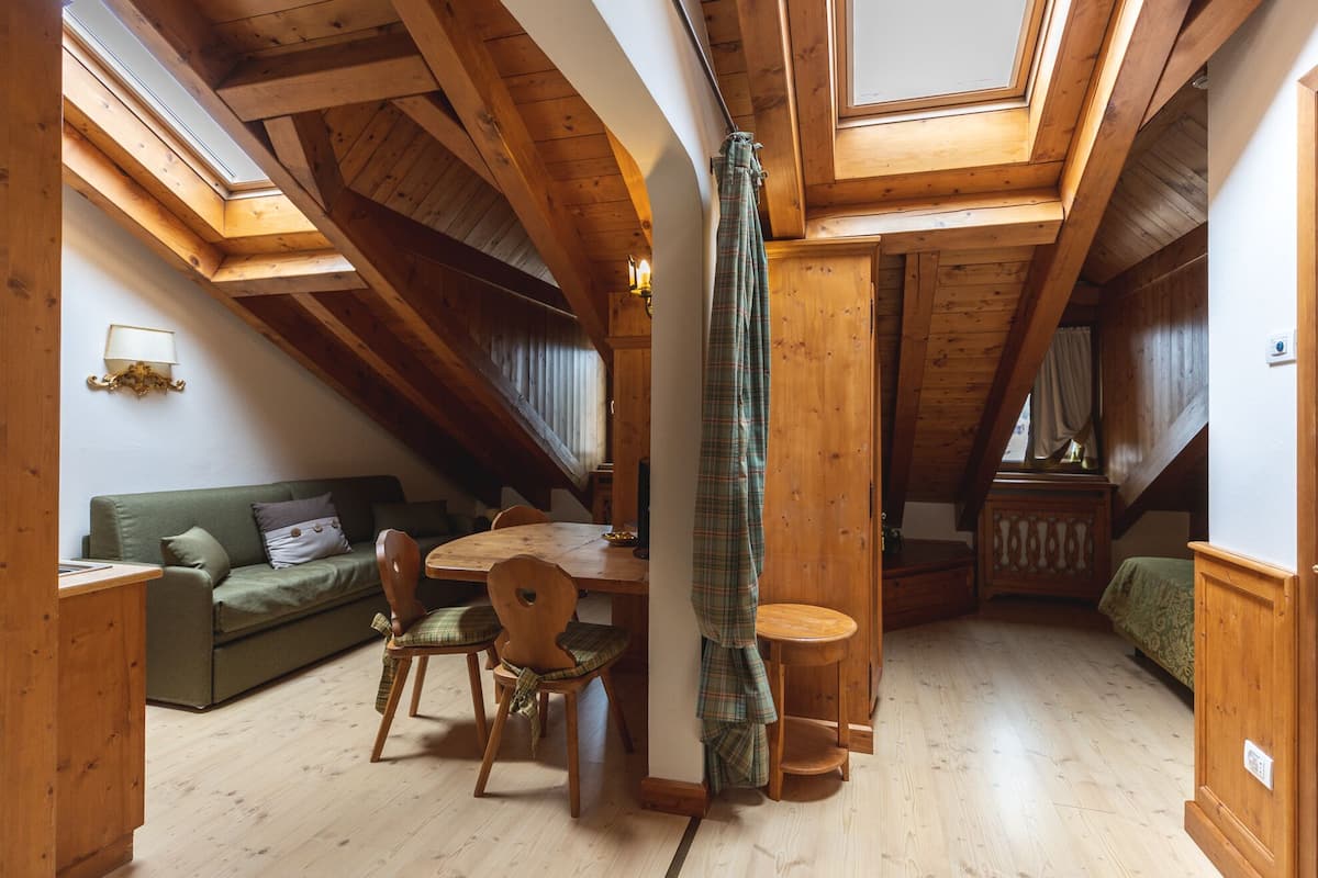 A cozy room with a wooden ceiling, a dining table with chairs, a sofa, and a window with curtains.