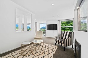 A modern living room with a sofa, armchair, and a TV mounted on the wall. - Central Queenstown Luxury (Queenstown)