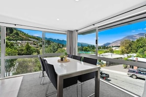 A modern room with a large window, a dining table with chairs, and a view of a mountainous landscape. - Central Queenstown Luxury (Queenstown)
