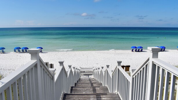 A wooden staircase leading to a beach with white railings and blue umbrellas. - Luxury Renovation in Seaside w/Expansive Rooftop Deck, Gulf Views, & 3 Kings (Santa Rosa Beach)