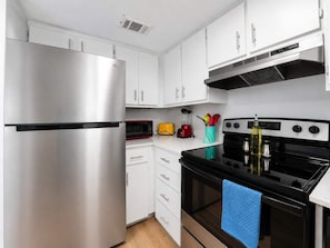 A modern kitchen with stainless steel appliances, white cabinets, and a black stove.
