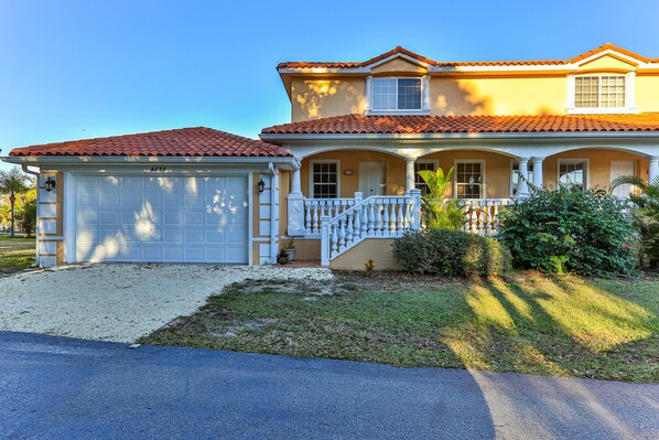 A two-story house with a red-tiled roof, a white garage, and a covered porch with white railings. - Tradewinds DEEP WATER 4Br3.5Ba Kayaks/Pr. Dock (Homosassa)