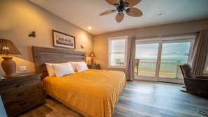 A bedroom with a bed, wooden headboard, bedside tables, lamps, a ceiling fan, a large window with blinds, and a view of the beach. - BEACHFRONT, 5BR/5BA, Sleeps up to 12 w/ Elevator & Pool! (St. George Island)