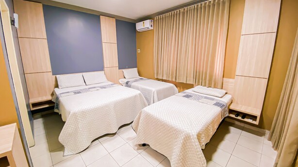 A hotel room with two beds, a ceiling light, an air conditioning unit, and a window with curtains.