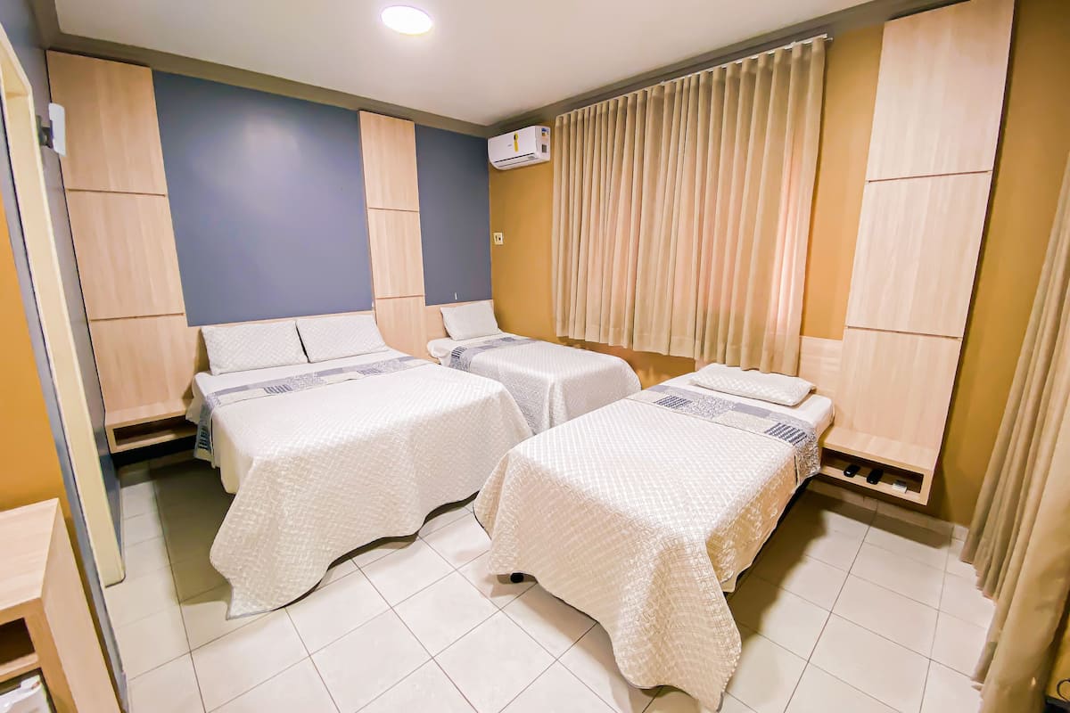 Ein Hotelzimmer mit zwei Betten, einer Deckenleuchte, einer Klimaanlage und einem mit Vorhängen versehenen Fenster.