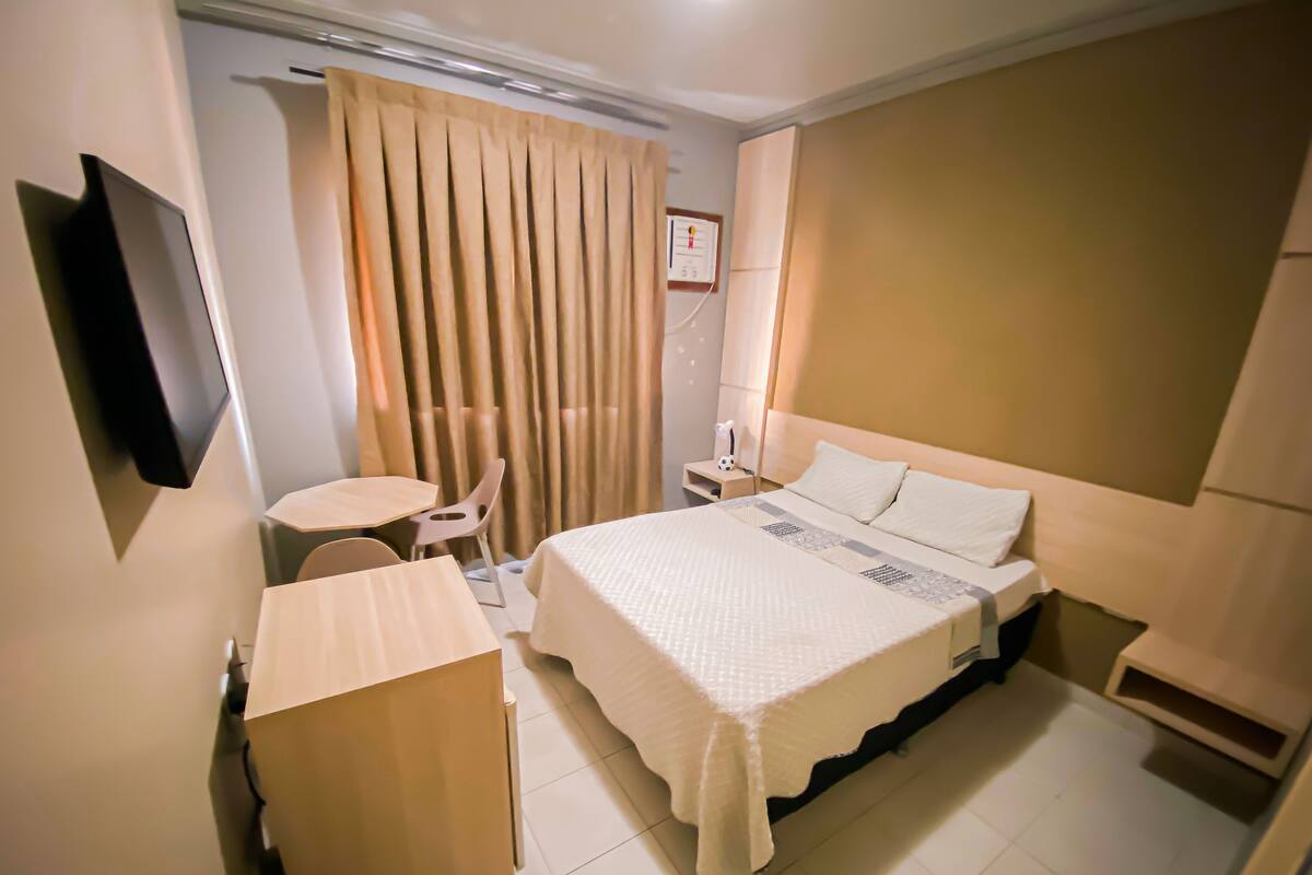 Ein Hotelzimmer mit Bett, Nachttisch, Stuhl und einem an der Wand befestigten Fernseher.