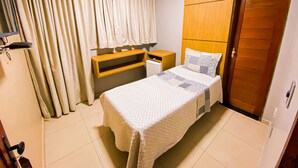 A bedroom with a bed, a wooden headboard, a nightstand, a bedside table, and a door.
