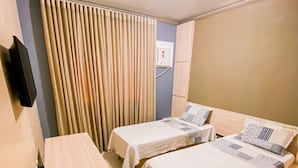 A hotel room with two single beds, a desk, a TV mounted on the wall, and a window with curtains.