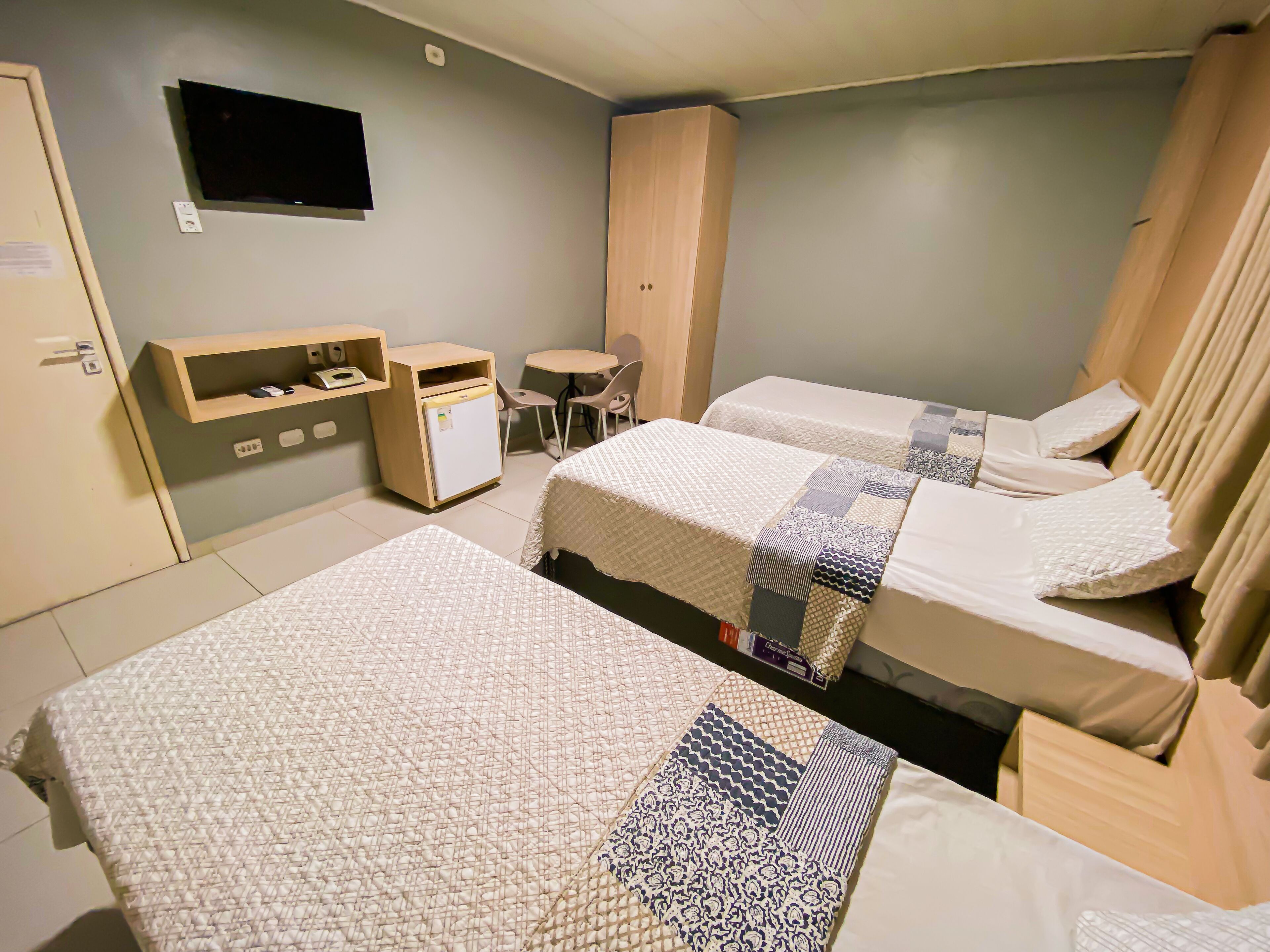 Une chambre d’hôtel avec deux lits, un bureau, une chaise, un petit réfrigérateur et un téléviseur fixé au mur.