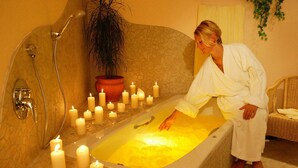 A bathtub with multiple candles, a shower, and a potted plant.