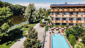 A hotel with a pool, a lake, and a forested area.