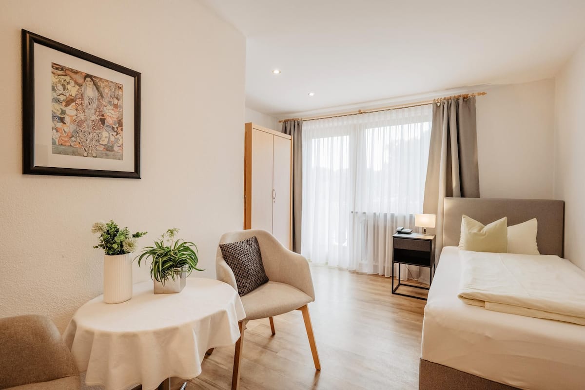 Une chambre d’hôtel avec un lit, une chaise, une petite table avec des plantes, un bureau et un tableau encadré au mur.