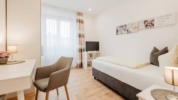 Una habitación de hotel moderna con cama, escritorio, silla, televisor y ventana con cortinas.