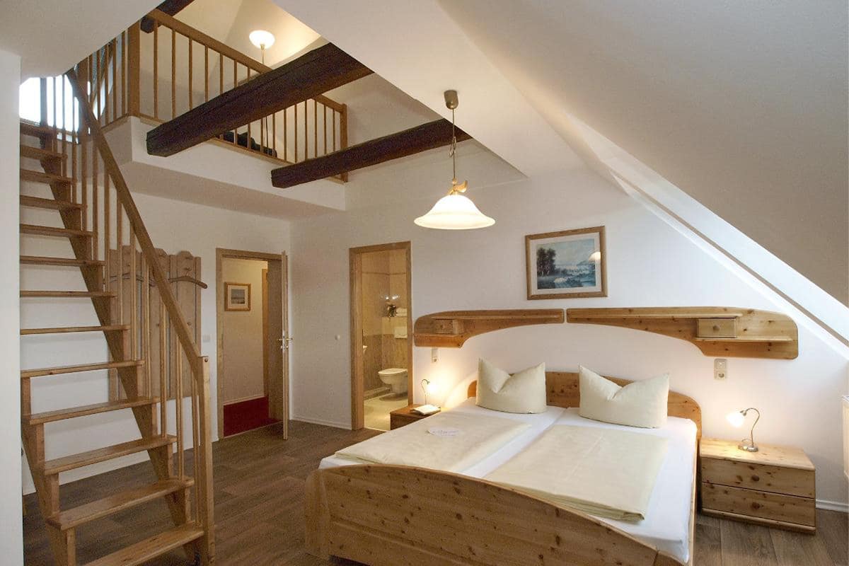 Une chambre avec un lit en bois, un escalier en bois, un luminaire au plafond et un tableau encadré accroché au mur.
