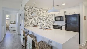 Una cocina moderna con una isla blanca, revestimiento de pared con estampado blanco y negro y un refrigerador negro.