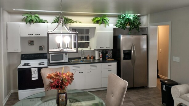 A modern kitchen with white cabinets, stainless steel appliances, and a glass dining table with a vase of flowers. - Beautiful Home in South Park. Walk to UD Campus, Miami Valley Hospital, Downtown (Dayton)