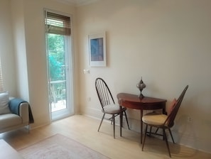 Un coin repas avec une table et des chaises, une fenêtre avec des stores, un tableau encadré au mur et un plancher de couleur claire.