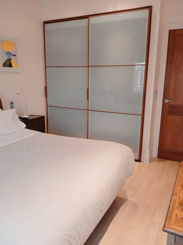 Un dormitorio con una cama, una mesita de noche, una puerta de madera y un armario correderas de vidrio.