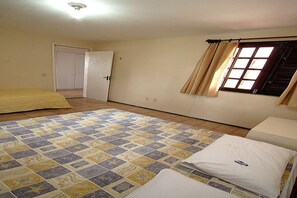 A room with a patterned floor, a bed with a white mattress and pillow, a window with curtains, and a door leading to another room.