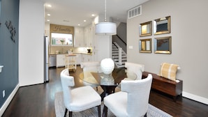A dining area with a glass table surrounded by white upholstered chairs, a wooden bench with a cushion, and a wall-mounted mirror.
