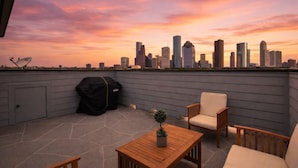A rooftop terrace with a city skyline view, a barbecue grill, and outdoor furniture.