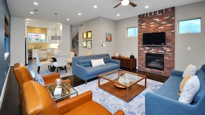 A spacious living room with a blue sofa, orange leather chairs, a coffee table, and a fireplace.