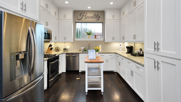 A modern kitchen with white cabinets, stainless steel appliances, and a window with a 'Humility' sign.
