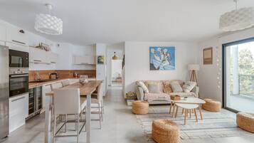 A modern kitchen with white cabinetry, stainless steel appliances, and a wooden dining table.
