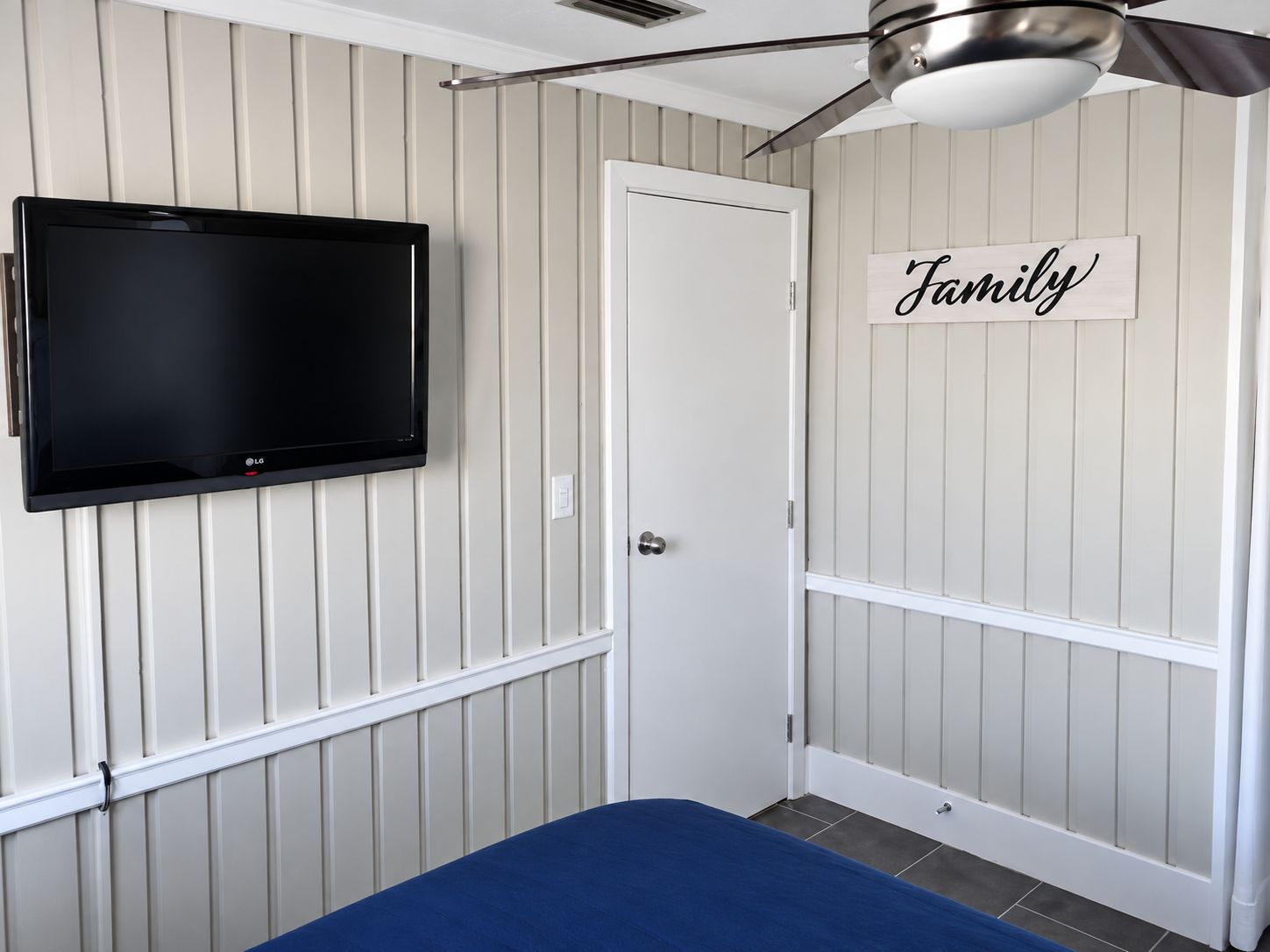 A bedroom with a bed, a television mounted on the wall, a ceiling fan, and a door with a 'Family' sign.
