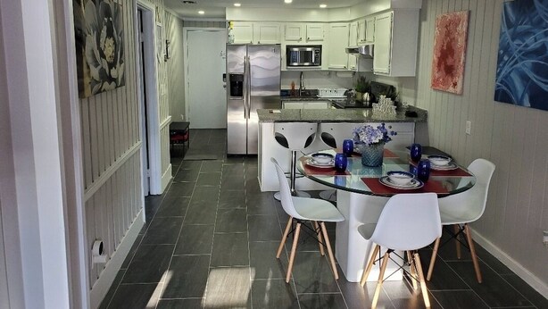 A modern kitchen with white cabinets, a central island, and a dining area with a glass table and white chairs.