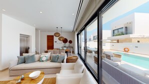 A modern living room with a large sofa, dining area, and a view of a pool. - Kalliopi is a contemporary villa, at Konnos Beach , within Periyiali Resort. (Protaras)